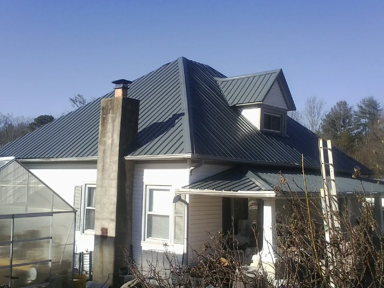Dark blue standing seam metal roof on a white farmhouse with dormer — Slate & Tile Roof Repair by Roofing Brothers in Sturgeon Bay