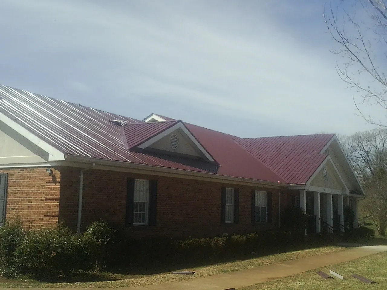Red metal roof with gabled entries on a long brick building, from a Hail Damage Roof Repair job in Sturgeon Bay
