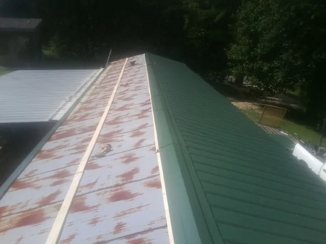 Old rusted panels beside newly installed green metal roofing — Wind Damage Roof Repair by Roofing Brothers in Sturgeon Bay