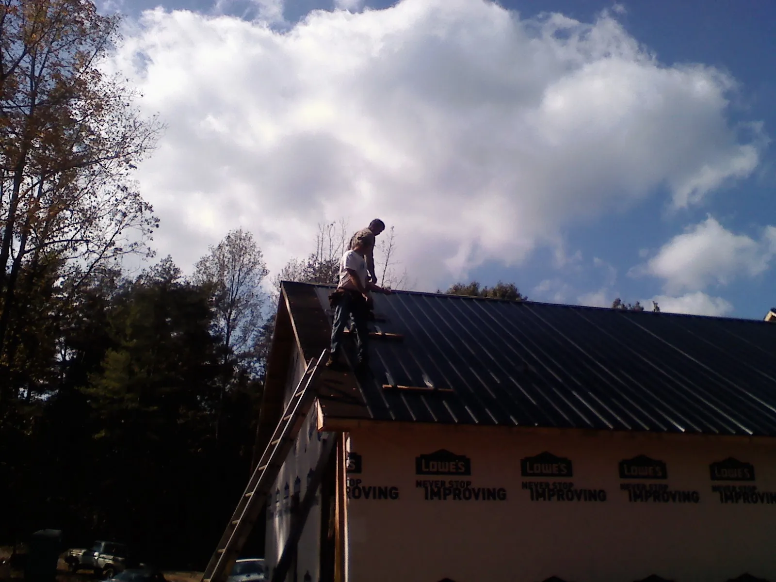 Roofer fastening dark metal panels high against a cloudy sky, from a Roof Inspection job in Sturgeon Bay