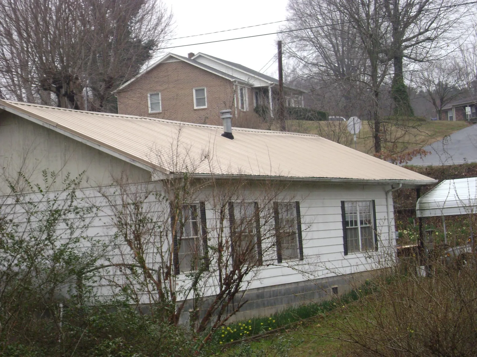 Tan metal roof on a white sided house set into a hillside — Commercial Roofing by Roofing Brothers in Sturgeon Bay