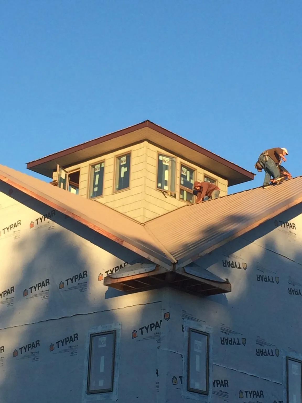 Roofers working around a rooftop cupola on a new metal roof at sunset — Roof Waterproofing in Sturgeon Bay by Roofing Brothers